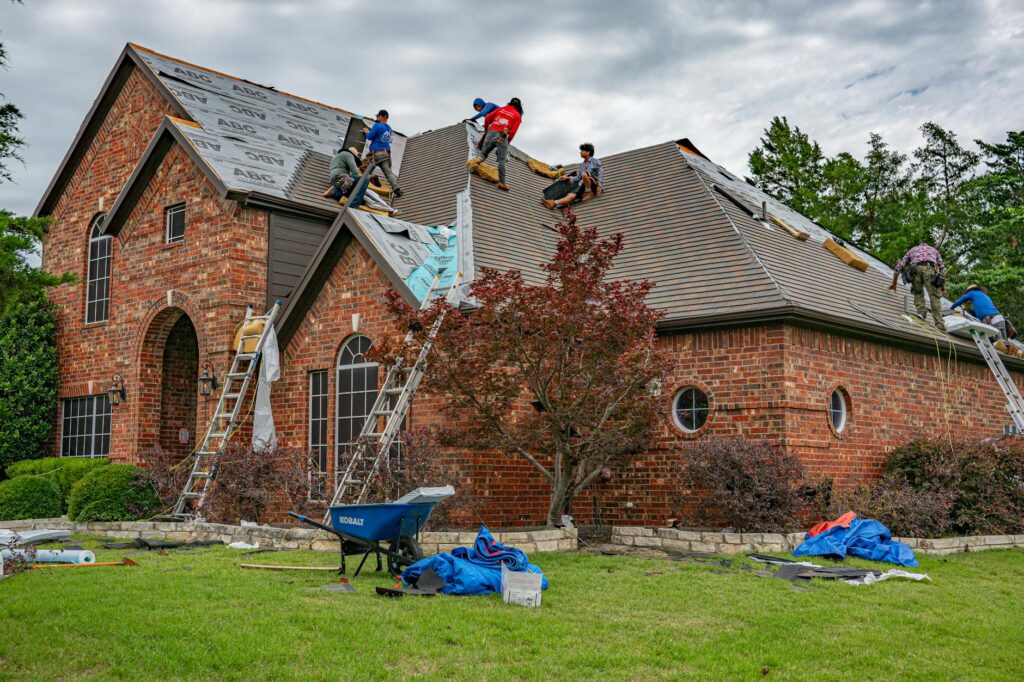 Roofers working on the shingled roof of a brick home