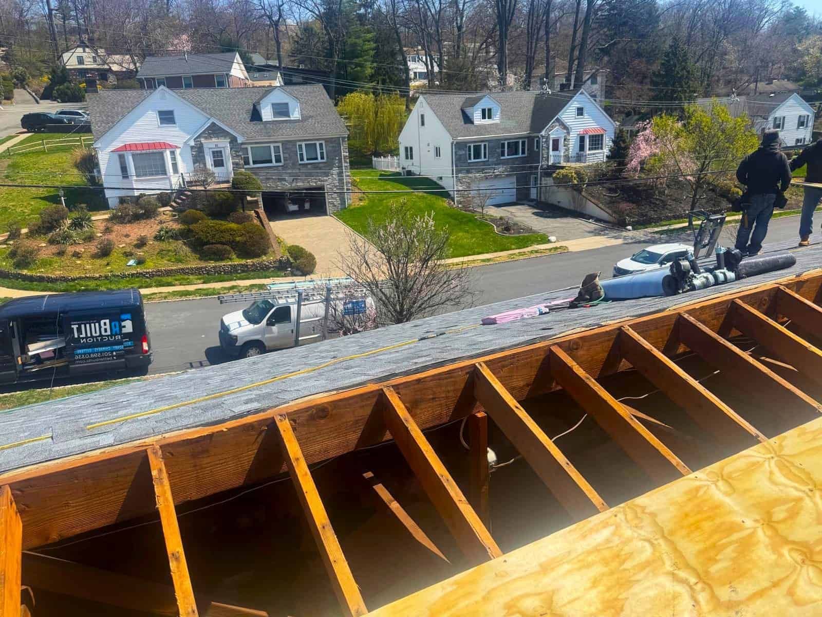 View from a New Jersey roof under repair, with Better Build Construction crew members and work vans on the street below